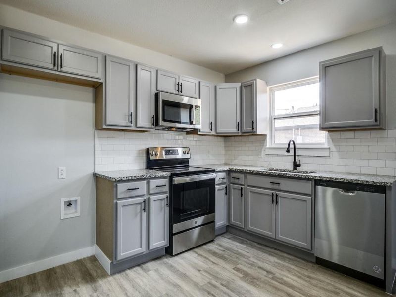 Kitchen featuring appliances with stainless steel finishes, backsplash, light wood-type flooring, and sink Kitchen featuring appliances with stainless steel finishes, backsplash, light wood-type flooring, and sink