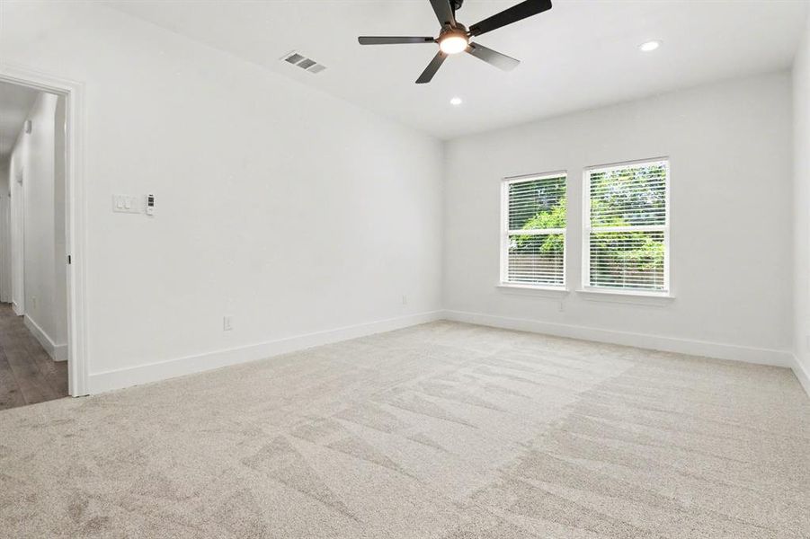 Spacious room featuring light-colored carpeting, two windows with blinds, recessed lighting, and a ceiling fan