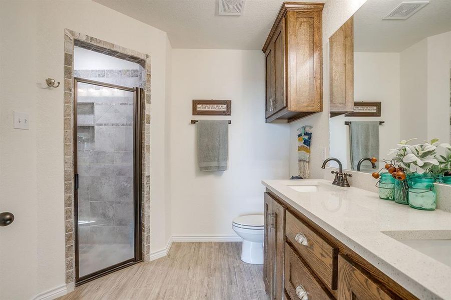 Primary bathroom with a stall shower, double vanity, and light wood-style tile flooring Primary bathroom with a stall shower, double vanity, and light wood-style tile flooring