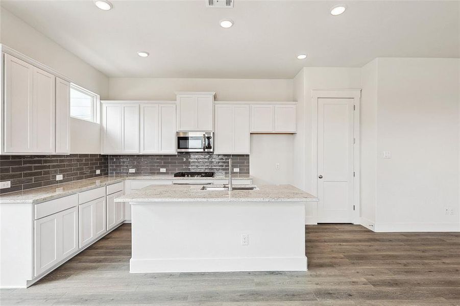 Kitchen with white cabinetry, backsplash, hardwood / wood-style flooring, and an island with sink