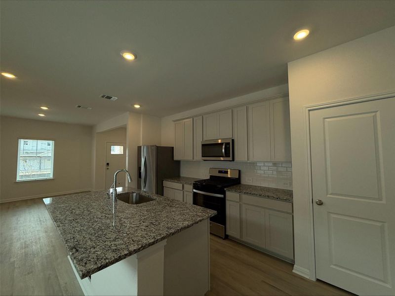Kitchen with appliances with stainless steel finishes, light stone countertops, tasteful backsplash, recessed lighting, and a kitchen island with sink