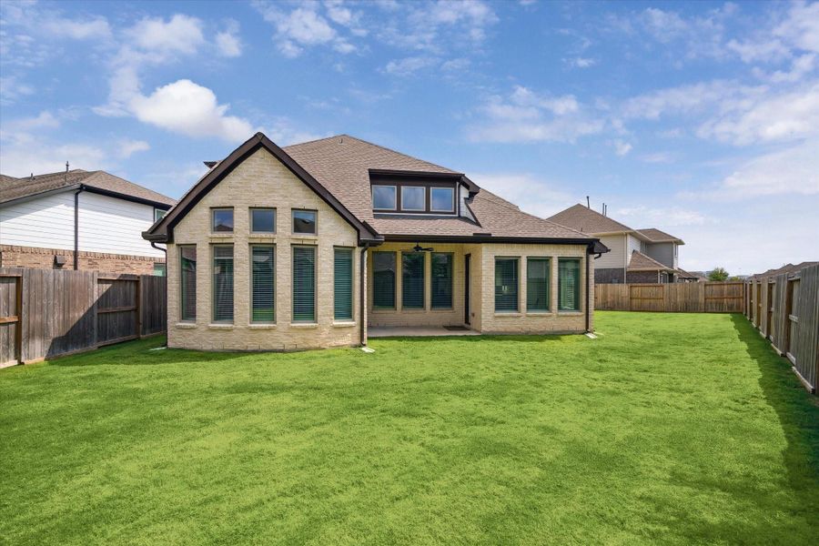 The rear elevation mirrors the home’s brick-and-stone front, featuring a covered patio with a ceiling fan—perfect for enjoying quiet mornings or relaxing evenings outdoors.