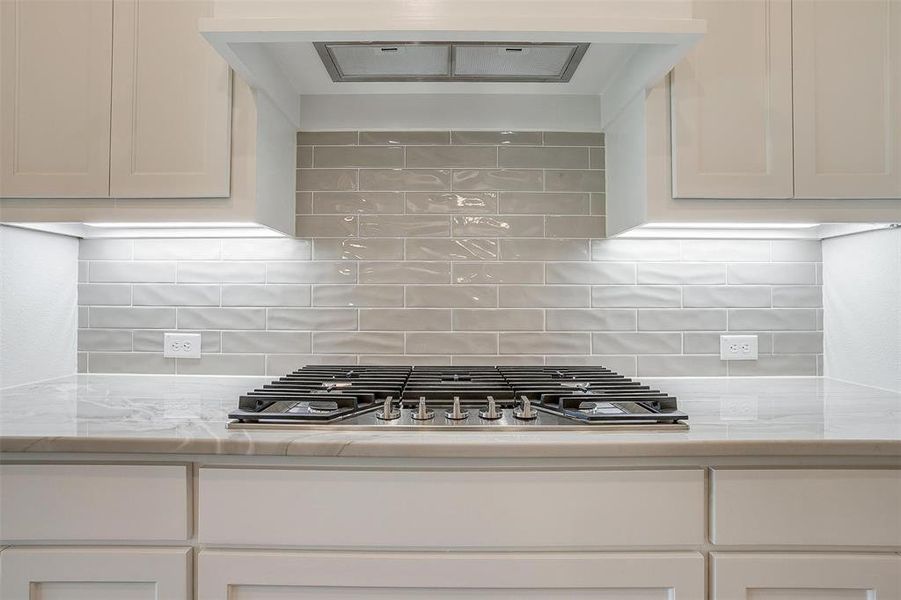 Kitchen featuring stainless steel gas cooktop, light stone countertops, decorative backsplash, and white cabinets