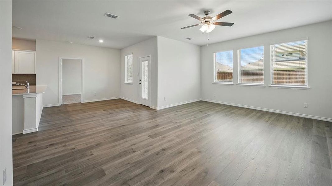 Spacious living area featuring wood-finish flooring, a ceiling fan, and three large windows with blinds