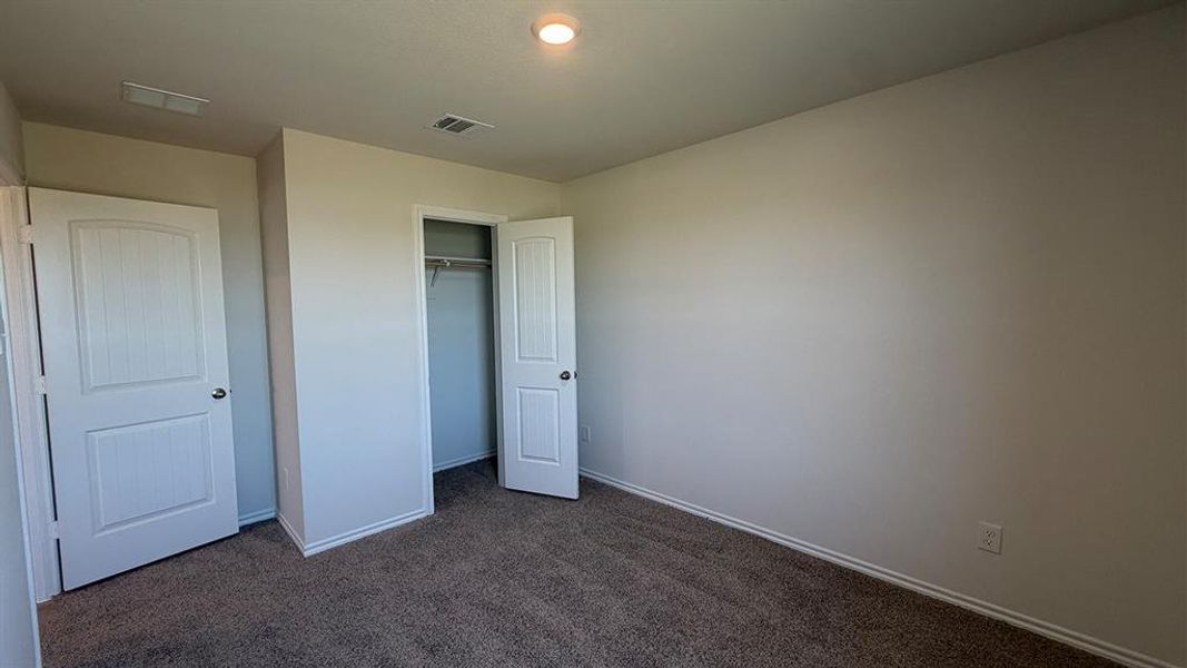 Spacious room featuring neutral carpeting, a built-in closet with hanging rod, white interior doors, and a ceiling-mounted light fixture