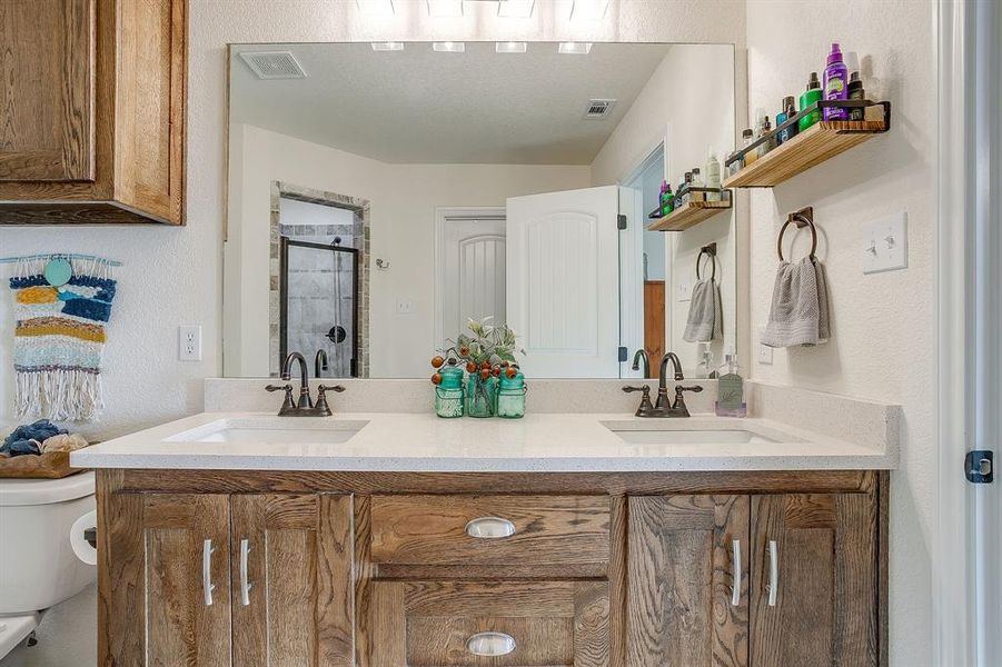 Primary bathroom featuring a textured wall, a shower stall, and double vanity Primary bathroom featuring a textured wall, a shower stall, and double vanity
