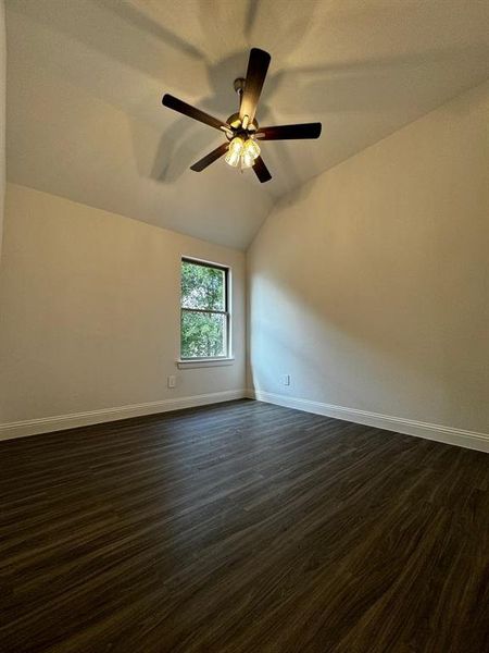 Empty room featuring ceiling fan, lofted ceiling, and dark wood-type flooring