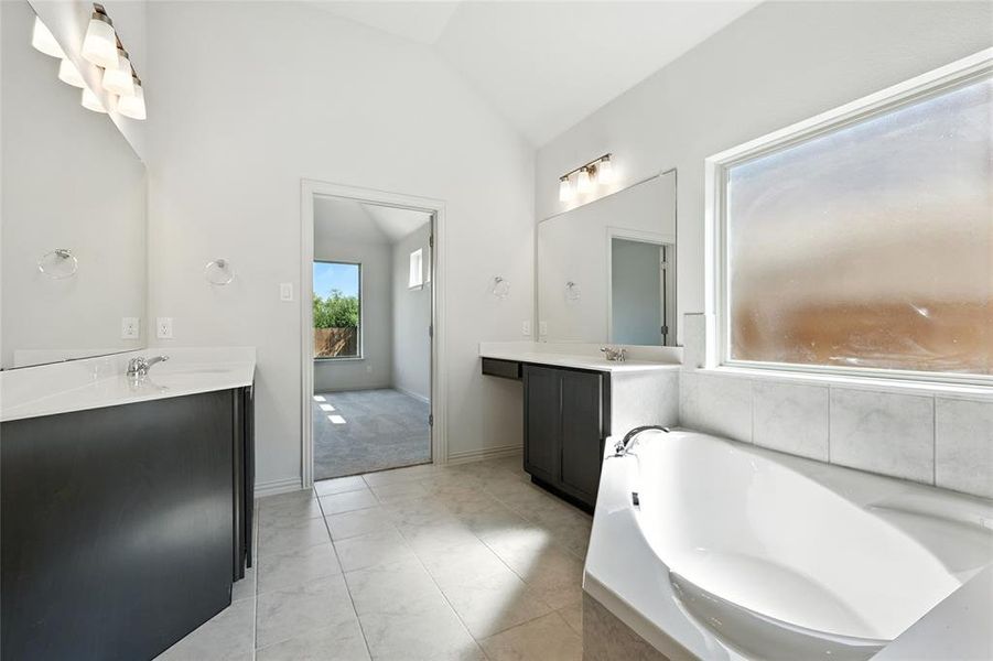 Bathroom featuring vaulted ceiling, two vanities, and a garden tub Bathroom featuring vaulted ceiling, two vanities, and a garden tub