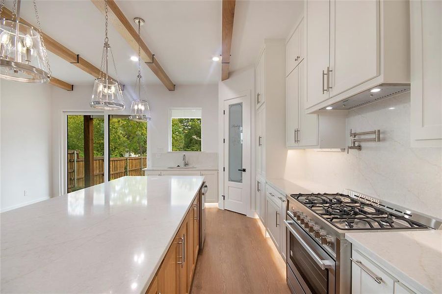 Kitchen featuring stainless steel gas range, light stone countertops, light wood-type flooring, hanging light fixtures, and white cabinets