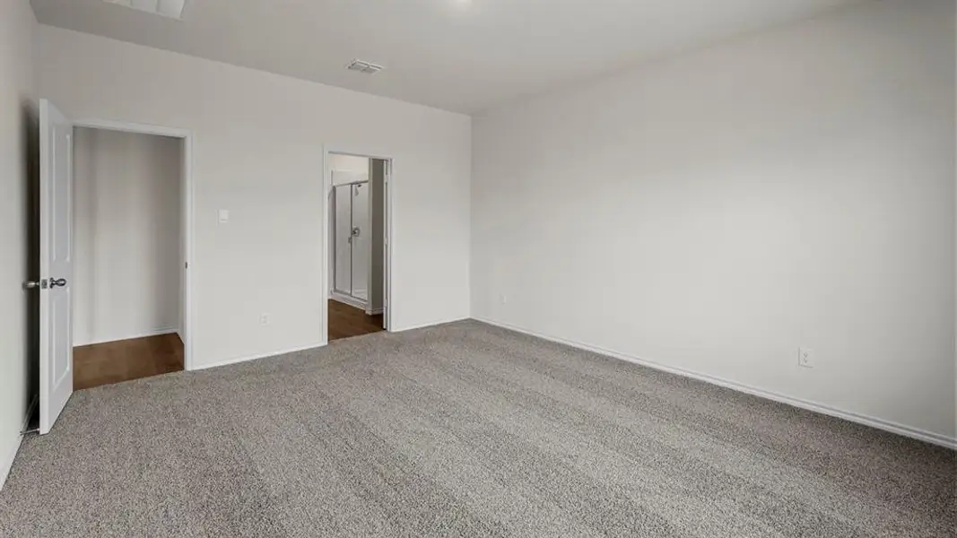 Spacious room featuring light grey carpet flooring and white walls, with a view into a bathroom with a shower enclosure