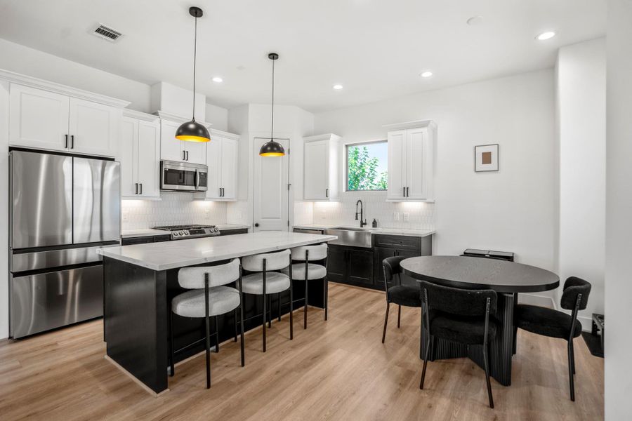 Bright, open kitchen meets chic dining—stainless steel appliances, crisp white uppers with matte-black pulls, and bold Iron Ore lowers for contrast.