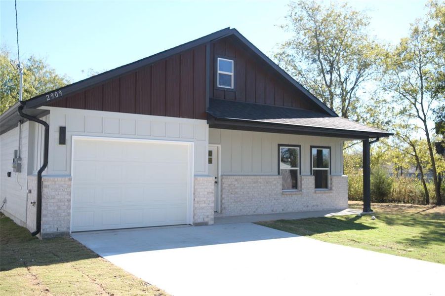View of front of home with brick siding, board and batten siding, a front lawn, an attached garage, and concrete driveway View of front of home with brick siding, board and batten siding, a front lawn, an attached garage, and concrete driveway