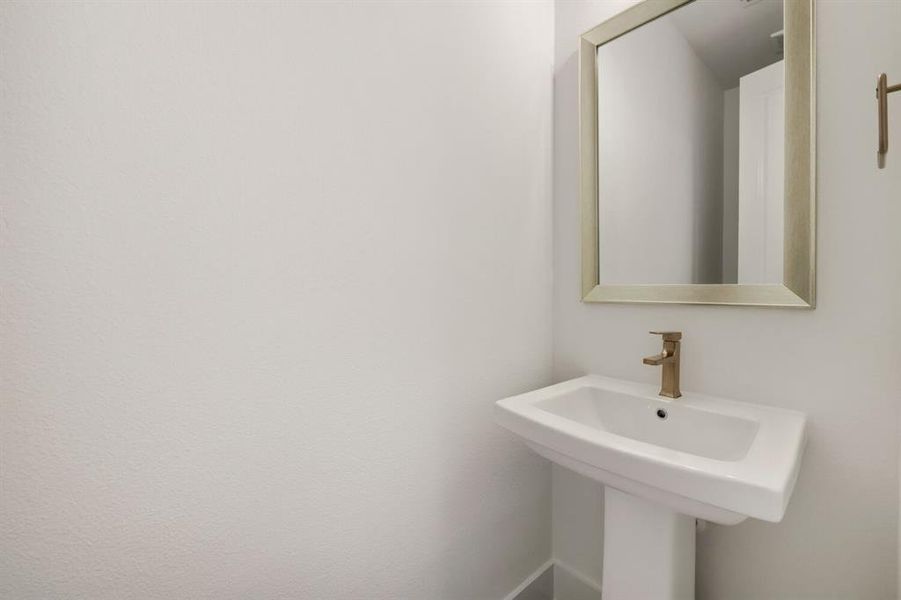 Pedestal sink with a gold-tone faucet, complemented by a framed mirror and a gold-tone towel bar Pedestal sink with a gold-tone faucet, complemented by a framed mirror and a gold-tone towel bar