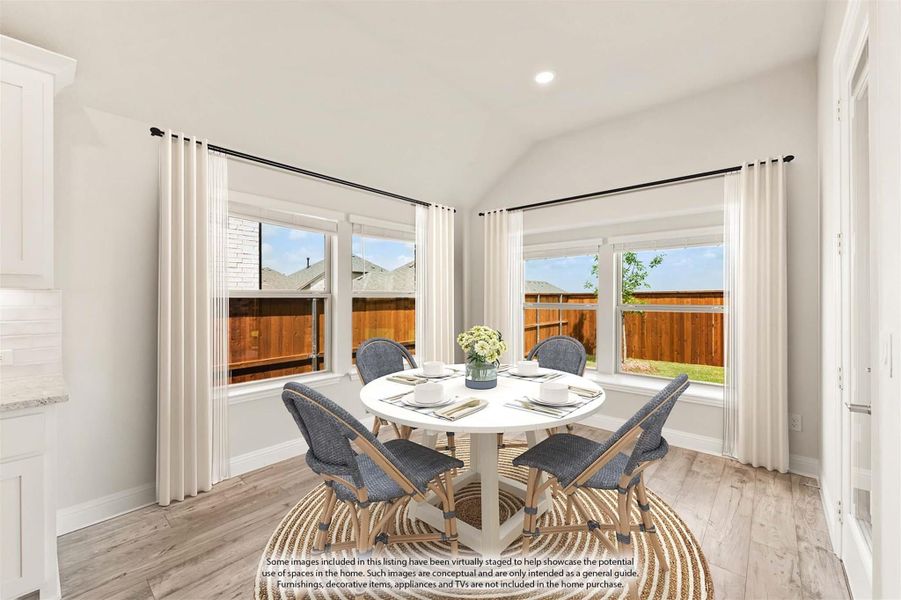 Bright dining area with round white table, four blue chairs, vaulted ceiling, and large windows overlooking backyard Bright dining area with round white table, four blue chairs, vaulted ceiling, and large windows overlooking backyard