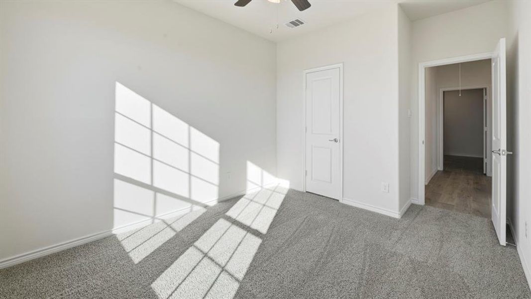 Spacious room featuring light gray carpeting, neutral wall finishes, a paneled door, and a ceiling fan