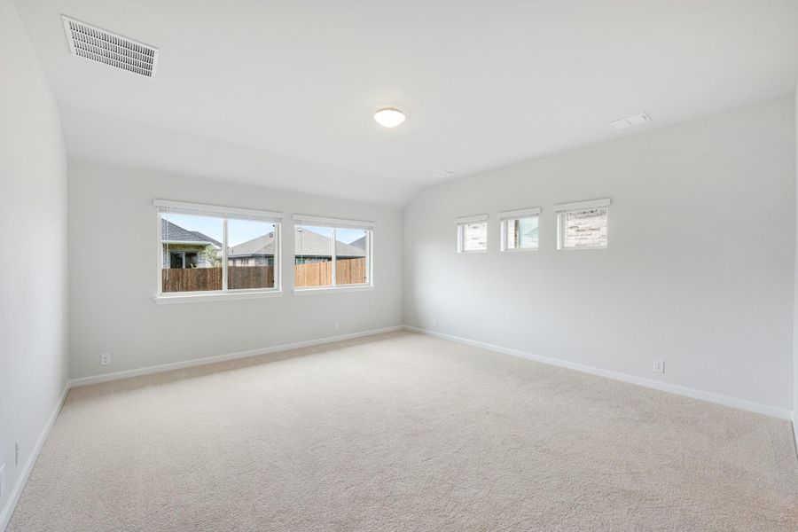 Empty bedroom with vaulted ceiling, beige carpet, and multiple windows along white walls