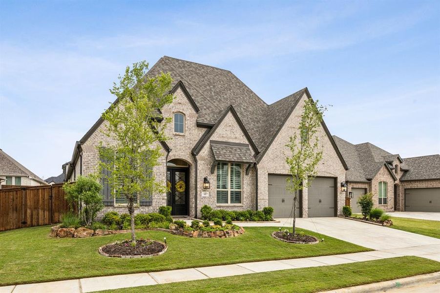 French country style house featuring brick siding, an attached garage, a shingled roof, and driveway
