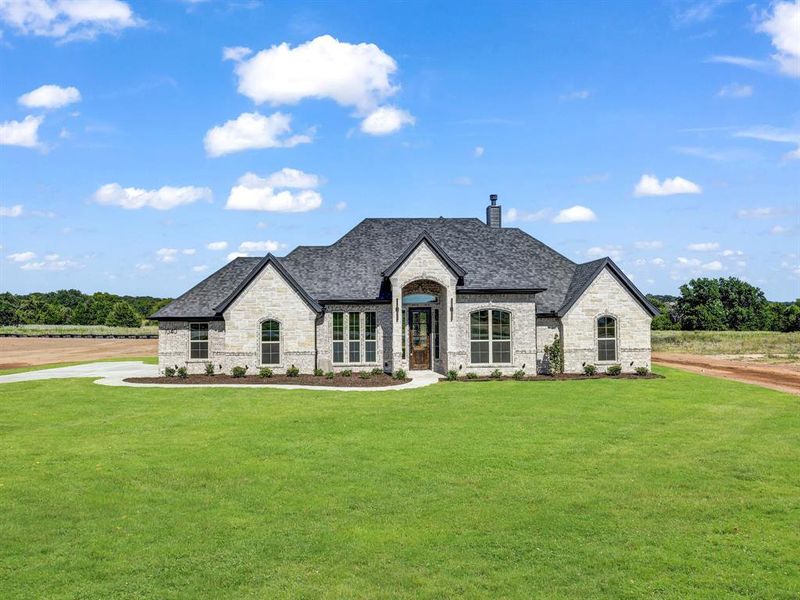 French country home featuring stone siding, a front lawn, a chimney, and brick siding French country home featuring stone siding, a front lawn, a chimney, and brick siding