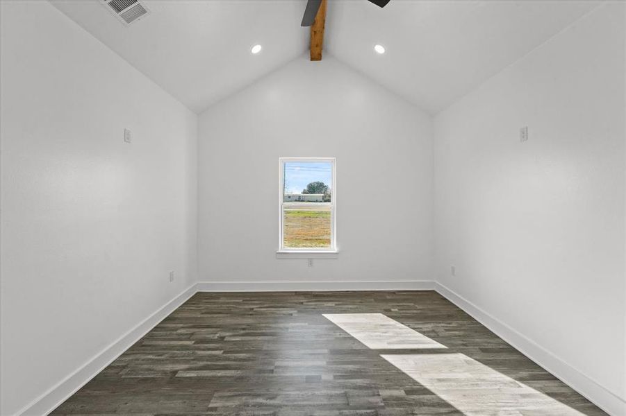 Spare room with ceiling fan, vaulted ceiling with beams, and dark hardwood / wood-style flooring