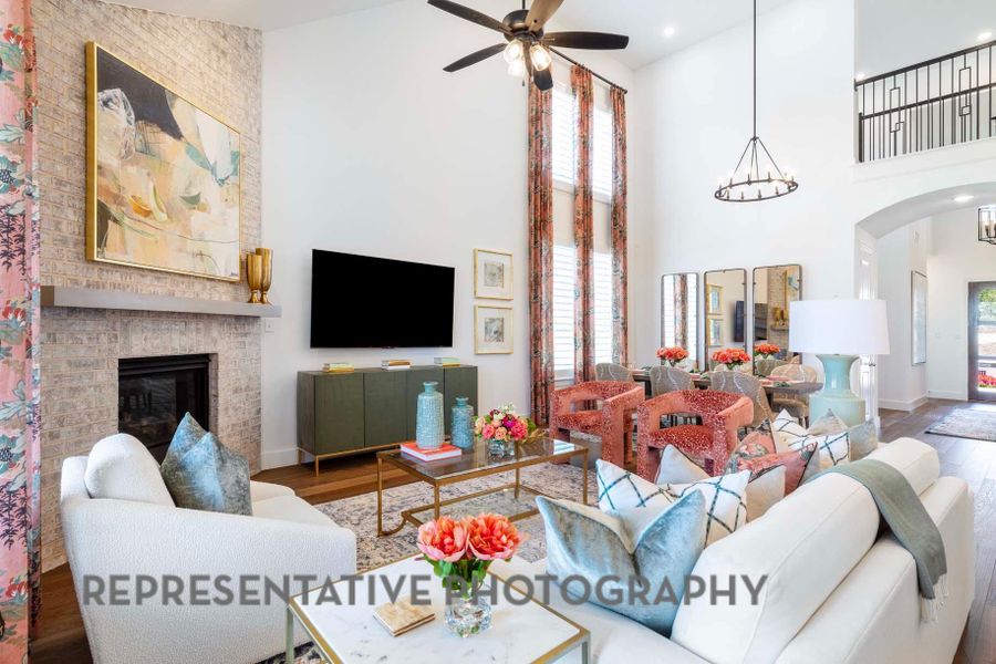 Living room featuring a towering ceiling, wood finished floors, ceiling fan with notable chandelier, and a brick fireplace Living room featuring a towering ceiling, wood finished floors, ceiling fan with notable chandelier, and a brick fireplace