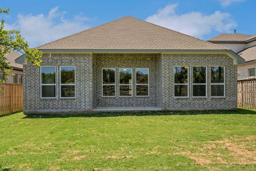 Back of house with a shingled roof, brick siding, fence, and a lawn