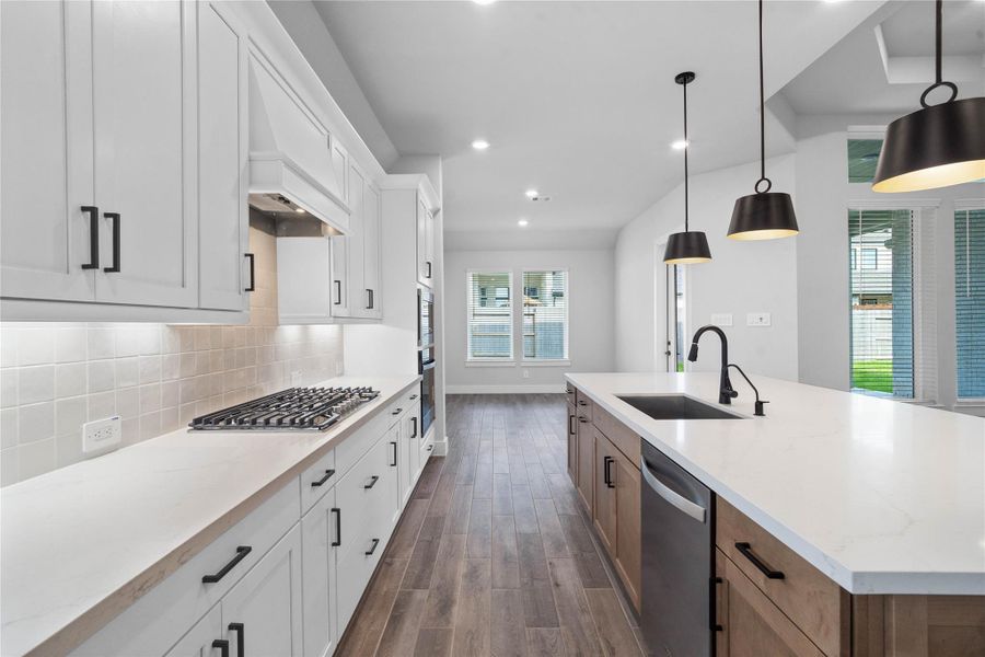 This modern kitchen showcases the premium finishes, dual-tone cabinetry, and bright open layout. Featuring white quartz countertops, built-in gas cooktop with matching range hood, under-cabinet backsplash, and mate black hardware.