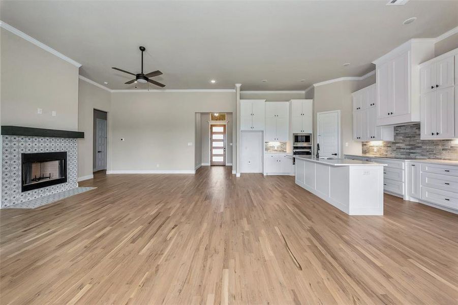 Kitchen featuring a tile fireplace, light hardwood / wood-style flooring, white cabinets, and an island with sink