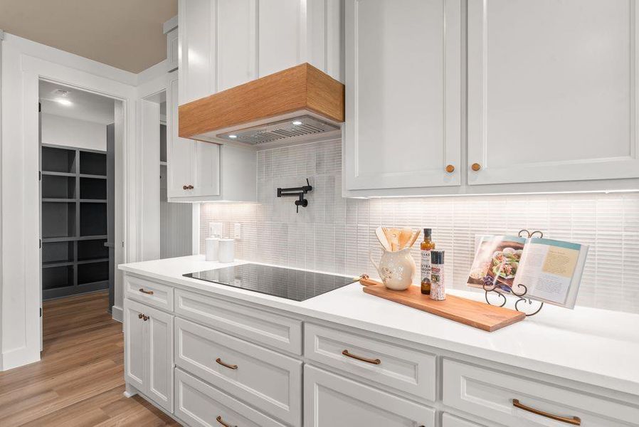 Kitchen with backsplash, white cabinets, black electric stovetop, light wood-style flooring, and light stone countertops Kitchen with backsplash, white cabinets, black electric stovetop, light wood-style flooring, and light stone countertops