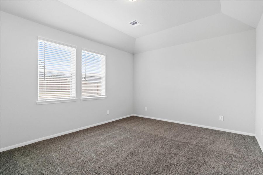 The primary bedroom provides a peaceful escape with a bright, neutral palette, sloped ceilings, large windows (fitted with blinds), and plush carpet flooring, creating a calm and restorative atmosphere to end your day.