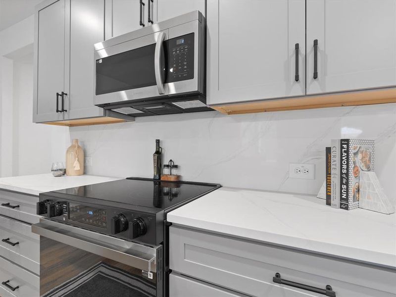Kitchen with light stone countertops, stainless steel microwave, black electric range, and tasteful backsplash Kitchen with light stone countertops, stainless steel microwave, black electric range, and tasteful backsplash