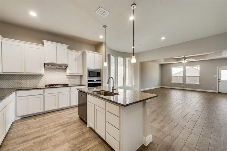 Kitchen with sink, a center island with sink, dark stone counters, pendant lighting, and stainless steel appliances