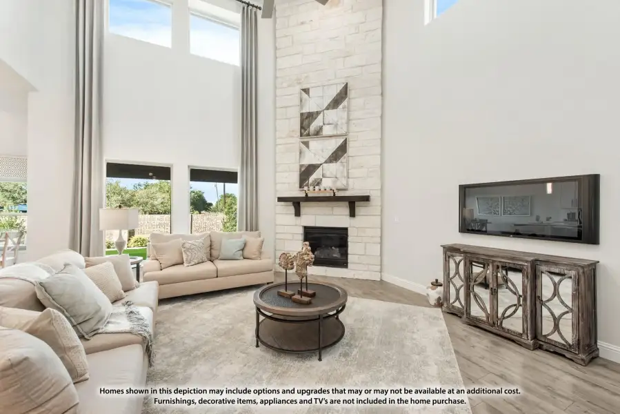 Living room with two-story stone fireplace, high ceilings, large windows, and neutral furniture on hardwood floors