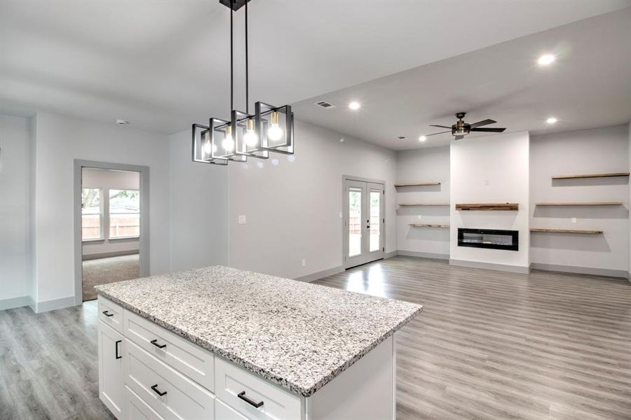 Kitchen with a kitchen island, light stone countertops, light wood-style flooring, pendant lighting, and recessed lighting Kitchen with a kitchen island, light stone countertops, light wood-style flooring, pendant lighting, and recessed lighting