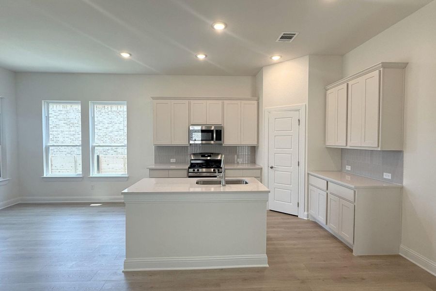 Kitchen featuring light-toned cabinetry, stainless steel appliances, a center island with an undermount sink, and light wood-finish flooring