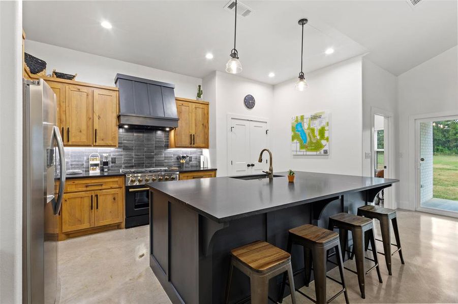 Kitchen featuring range with gas cooktop, an island with sink, stainless steel refrigerator with ice dispenser, a kitchen breakfast bar, and backsplash