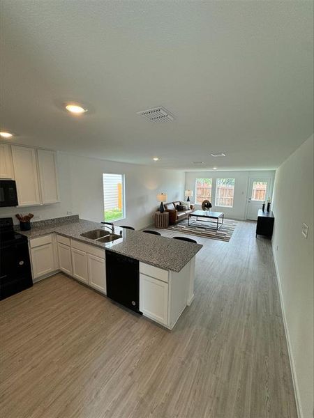 Kitchen featuring light wood-type flooring, kitchen peninsula, black appliances, and a wealth of natural light