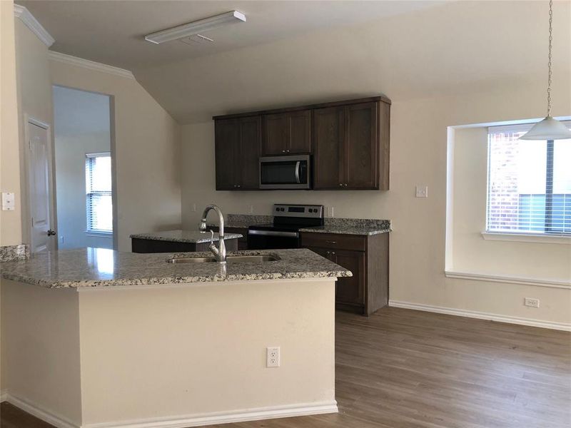 Kitchen featuring light stone countertops, dark brown cabinets, stainless steel appliances, sink, and pendant lighting