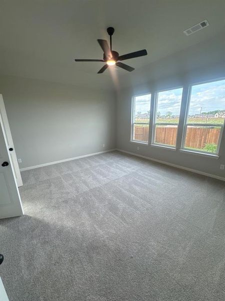 Spacious room with plush gray carpeting, three large windows, a ceiling fan with integrated lighting, and neutral wall tones