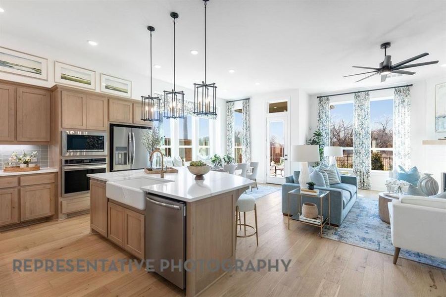 Kitchen with hanging light fixtures, a kitchen island with sink, light wood-style flooring, appliances with stainless steel finishes, and open floor plan