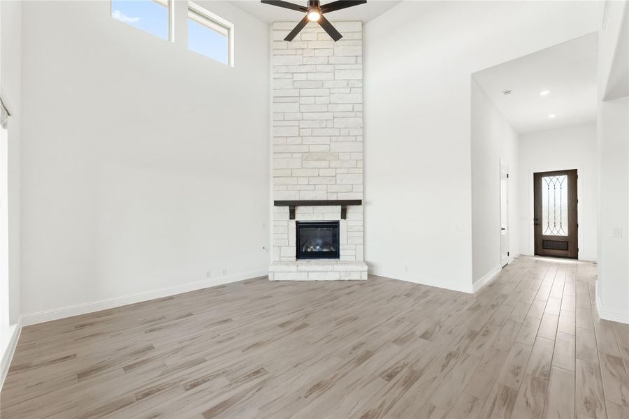 Open living room with floor-to-ceiling white brick fireplace, wood-look floors, and ceiling fan Open living room with floor-to-ceiling white brick fireplace, wood-look floors, and ceiling fan