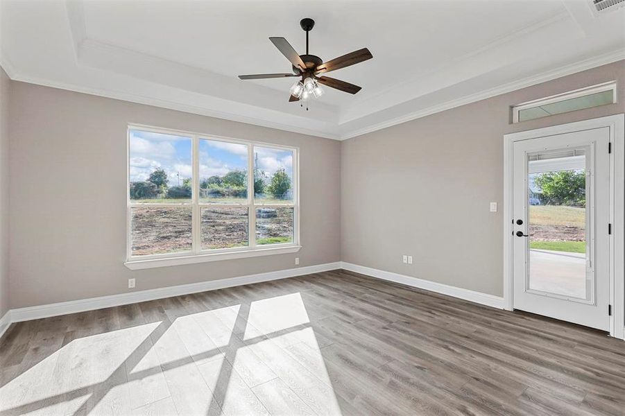 Empty room with light wood-type flooring, crown molding, and a tray ceiling