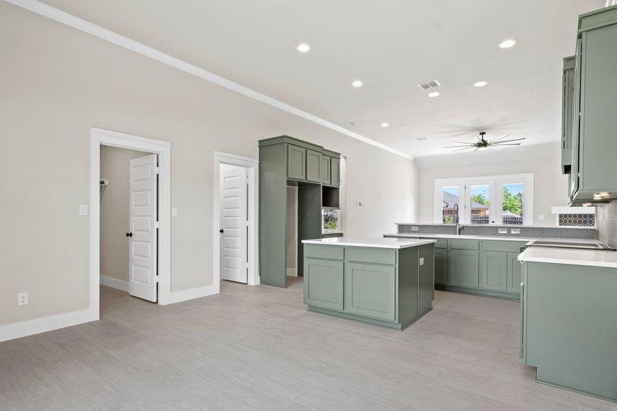 Kitchen with green cabinets, ornamental molding, a ceiling fan, a kitchen island, and light wood-style floors Kitchen with green cabinets, ornamental molding, a ceiling fan, a kitchen island, and light wood-style floors