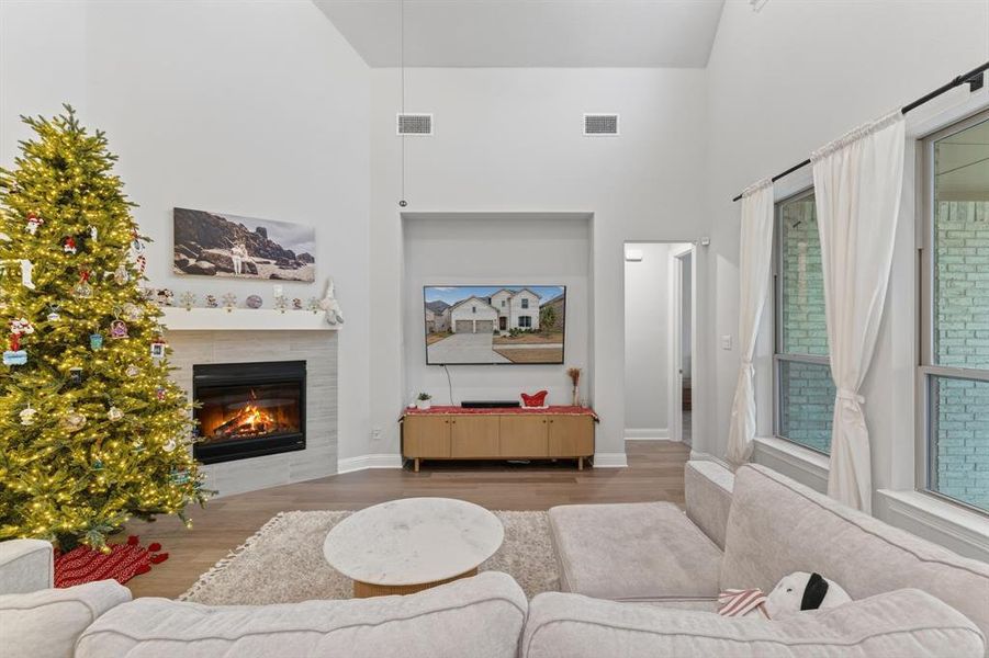 Living area featuring a high ceiling, a tiled fireplace, and wood finished floors Living area featuring a high ceiling, a tiled fireplace, and wood finished floors