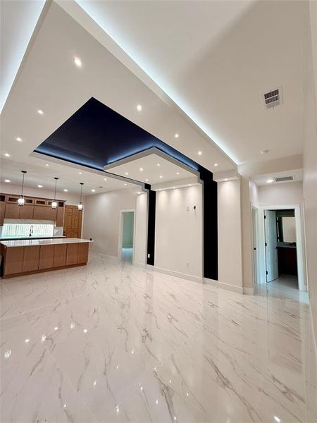 Unfurnished living room with a raised ceiling, baseboards, recessed lighting, and light marble finish flooring