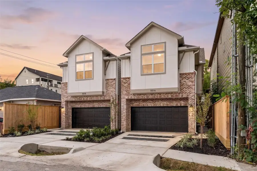Impressive curb appeal — warm dusk exterior lighting, dual private garage entries, custom perimeter fencing, and decorative stone-accented driveway pads.