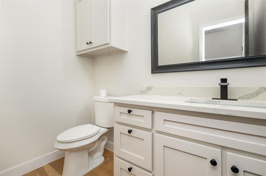 Bathroom featuring vanity, toilet, wood finished floors, and baseboards