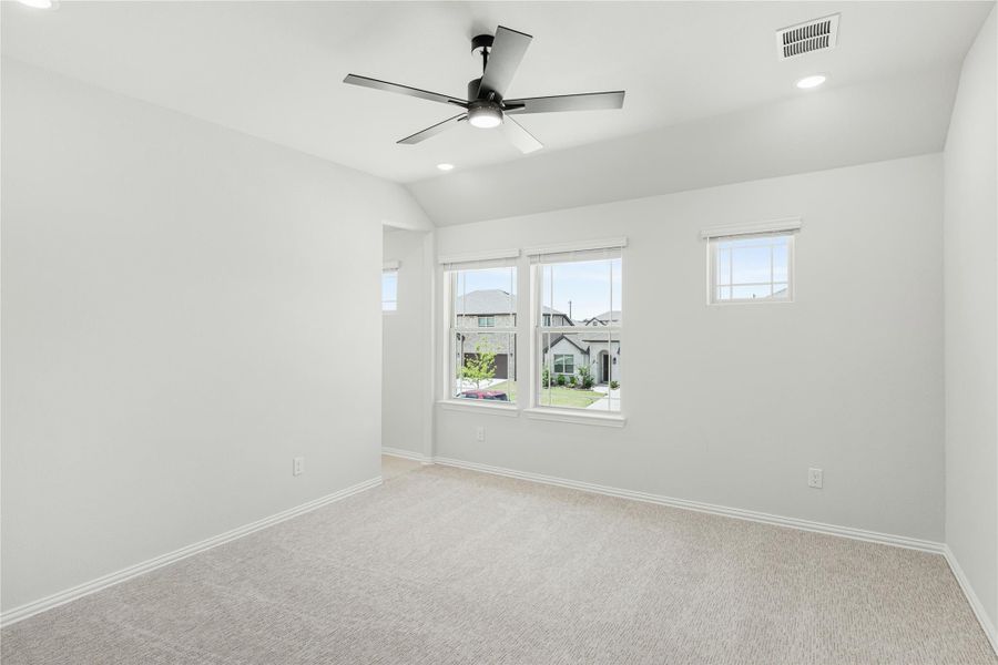 Empty bedroom with carpet flooring, ceiling fan, vaulted ceiling, and windows overlooking neighborhood homes