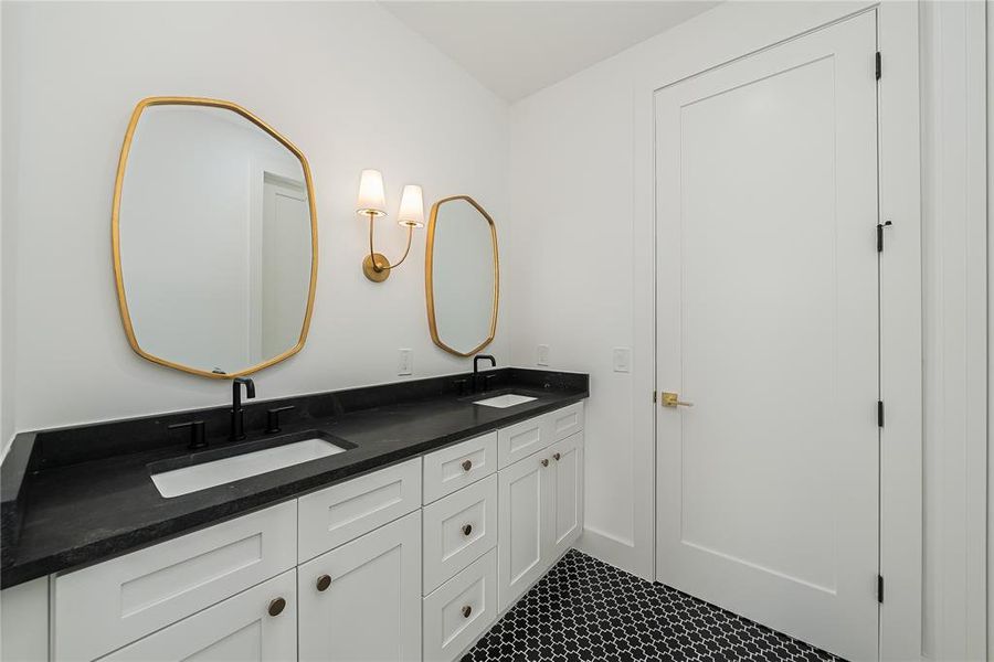 Bathroom featuring a dual vanity with a dark countertop, two framed mirrors, and a patterned floor