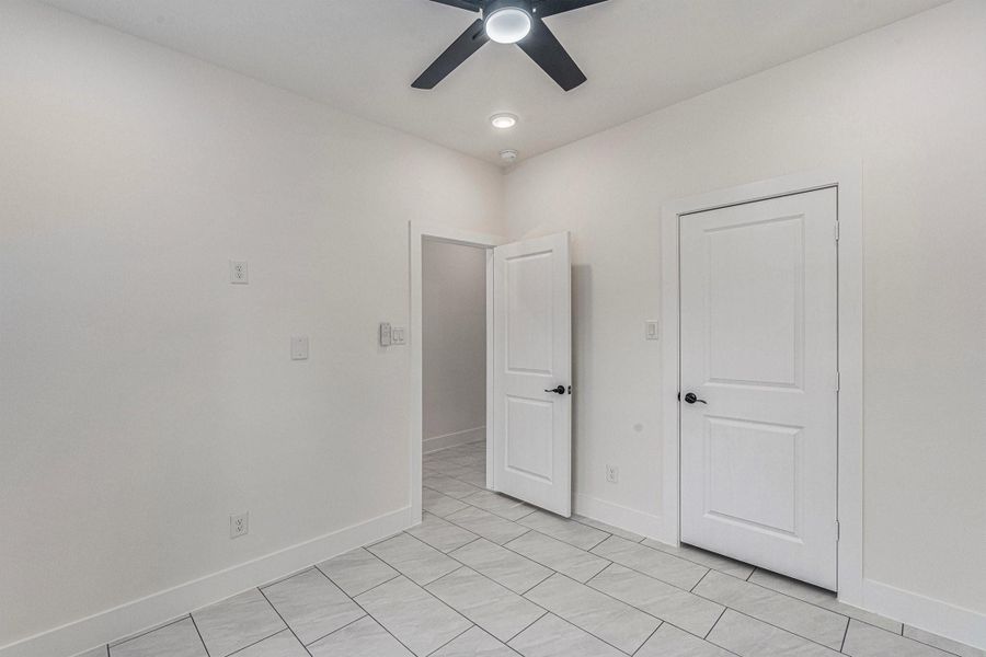 This room features clean white walls and tiled flooring, with a modern ceiling fan and recessed lighting. It includes two doors, one likely leading to a closet, and offers a bright, minimalist space.