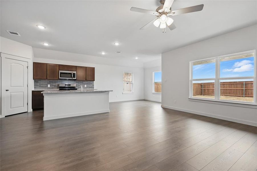 Kitchen featuring a center island with sink, dark wood finish cabinetry, a ceiling fan, light stone countertops, and tasteful backsplash Kitchen featuring a center island with sink, dark wood finish cabinetry, a ceiling fan, light stone countertops, and tasteful backsplash